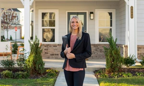 A friendly real-estate agent greets buyers in front of a home for sale